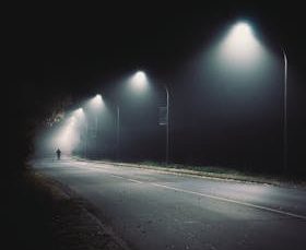 Silhouette of a person walking under streetlights on a foggy night in Coesfeld, Germany.